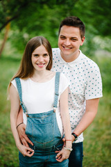 Obraz premium Pregnant girl and her husband are happy to hug, hold hands on stomach, stand in the outdoor in the garden background green. Close up. upper half. looking at camera