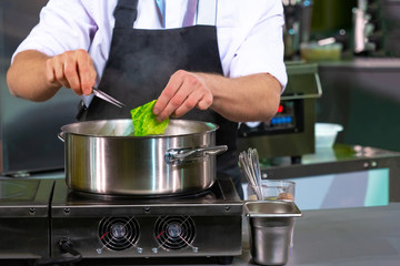Cook removes the cabbage leaf from the pan. Cooking cabbage. Cook checks the readiness. Dish with the addition of a leaf of salad. Chef works with tweezers. Cooking broth. Chef courses