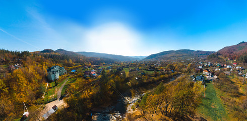 Aerial panoramic view of the village of Sheshory, surrounded by the Carpathian mountains. Buildings and infrastructure. The nature of Ukraine. Sunny autumn day. Huk waterfall on the Pistynka River. - obrazy, fototapety, plakaty