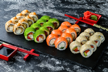 Set of sushi rolls with salmon on dark stone served with ginger and wasabi and wooden black wooden table. Fresh Japanese cuisine. Close up view on asian food. Sushi image for menu.