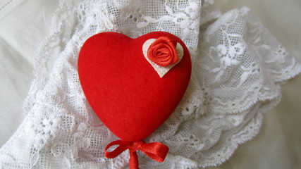 A red heart on a stick with a small red bow, decorated with a small red rose, lying on white lace panties. Saint Valentine's Day gift concept. 