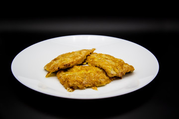 White plate with chops with meat on a black background. Fried meat in an egg on a plate. Three fried chops
