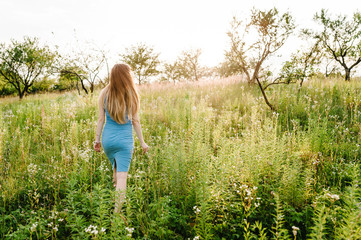 Beautiful Pregnant girl in stylish summer dress walking in  field with flowers in sunlight, enjoying freedom feeling.  full length. go back.