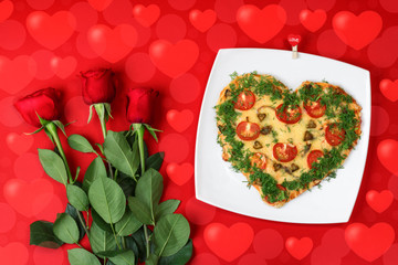 Valentine's day food. Heart shaped pizza next to a red roses, on a red background, with bokeh of heart. Valentine's day concept. Top view. Copy space