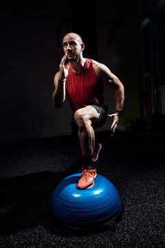 Fit athlete performing exercise on gymnastic hemisphere bosu ball on dark studio.