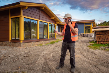 Builder calls the customer. Man frowns and talks on the phone. Architect discusses the estimate. Builder with papers and a phone in hands. Conversation with the customer of the construction.