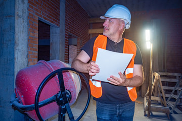 Builder next to a concrete mixer. Architect on a construction site. Man leaned on a concrete mixer....