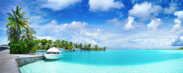 White Boat at pier with palm trees, Maldives island. Beautiful panoramic tropical landscape with turquoise ocean and blue sky with clouds. - obrazy, fototapety, plakaty
