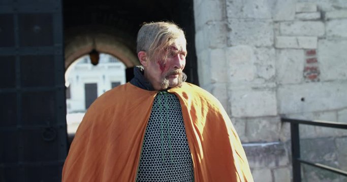 Old, wounded hetman in armor walks on fortress yard and looks around