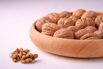 Walnuts heap food in wooden bowl on white background near to peeled nuts, angle view, healthy food concept