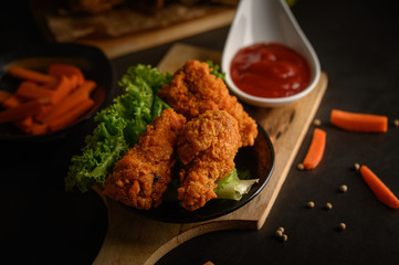 Crispy fried chicken on a cutting board with tomato sauce and carrot, Selective focus.