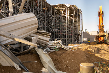 Parts of the ruins of a partially demolished high-bay warehouse with a demolition excavator in the...