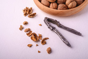 Walnuts heap food in wooden bowl with half peeled nut, cracked nutshell, near to vintage nutcracker on white background, angle view, healthy food concept