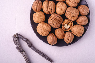 Walnuts heap food with half peeled nut in black plate near to vintage nut cracker on white background, top view, healthy food concept