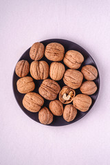Walnuts heap food in black plate with half peeled nut on white background, top view, healthy food concept