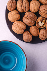 Walnuts heap food with half peeled nut in black plate near to empty blue bowl on white background, top view, healthy food concept