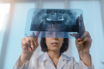 Close up picture of young woman doctor dentist who analysis dental x ray orthopantomogram. Dental panoramic radiography