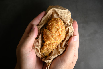 Crispy fried chicken on brown paper and put in hands.