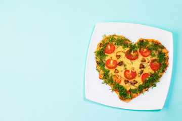 Valentines Day food. Heart shaped pizza with greens, on a pastel green or blue background. Top view. Copy space