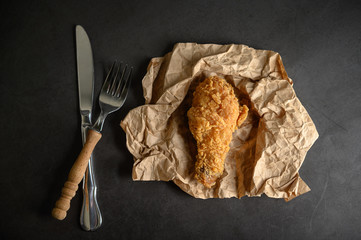 Crispy fried chicken on brown paper with a knife and fork.