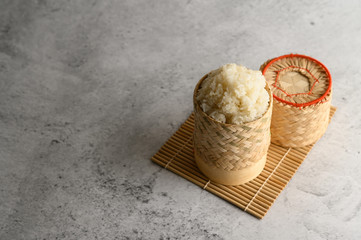 Thai sticky rice in a woven bamboo basket on a wooden panel.