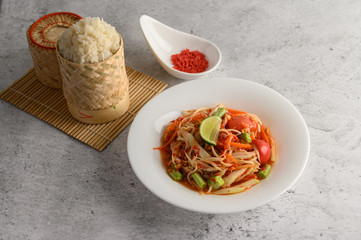 Thai papaya salad in a white plate with Sticky rice in wicker basket bamboo and dried shrimp.
