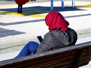 Muslim woman sitting on a bench looking at the cellphone