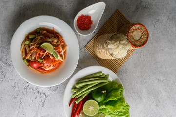 Thai papaya salad in a white plate with Sticky rice in wicker basket bamboo and dried shrimp.