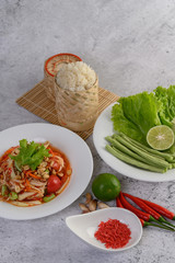 Thai papaya salad in a white plate with Sticky rice in wicker basket bamboo and dried shrimp.