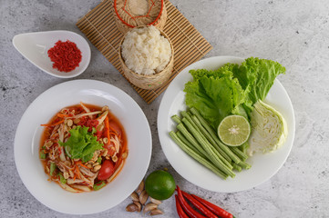 Thai papaya salad in a white plate with Sticky rice in wicker basket bamboo and dried shrimp.
