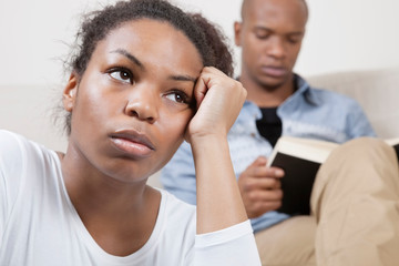 Sad young woman with man reading book in background