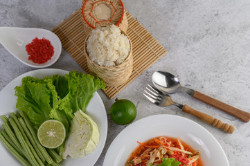Thai papaya salad in a white plate with Sticky rice, Spoon, fork, and dried shrimp.
