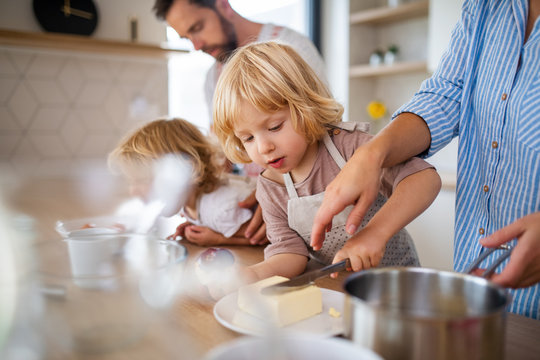 Young family with two small children indoors in kitchen, preparing food.