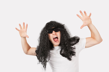 Portrait of young man with wig and sunglasses shouting against gray background