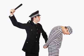 Side view of police officer with nightstick arresting male prisoner against gray background