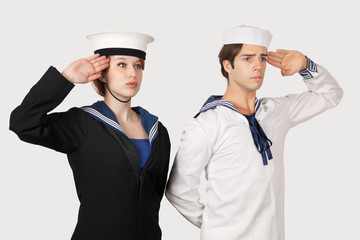 Young man and woman in sailor's uniform saluting against gray background