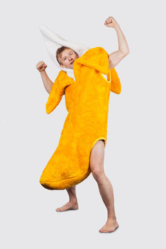 Portrait of young man in banana costume flexing muscle against gray background