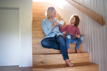A cute small girl with mother indoors at home, sitting on staircase.