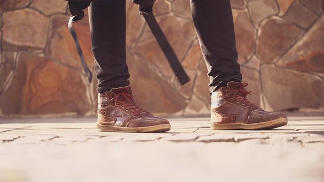 Unrecognizable men feets in sneakers is walking on tile road. He is holding a backback near his feet. Then other people are passing by. Cropped. Action. Animation. 4K.