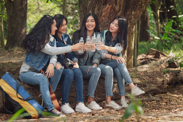 Group of Asian teenage girls camping in the forest and was sitting, relaxing, drinking water happily.