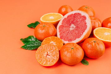 Fresh ripe mandarins, grapefruit and oranges with green leaves on orange background.