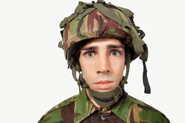 Close-up portrait of young soldier staring against gray background