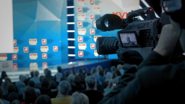 The cameraman makes video for television. Auditorium, seminar and lecture on business. Professional ideas, politics or economy. Energy gesturing in large room.