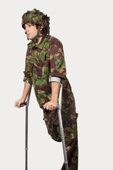 Young soldier holding crutches against gray background