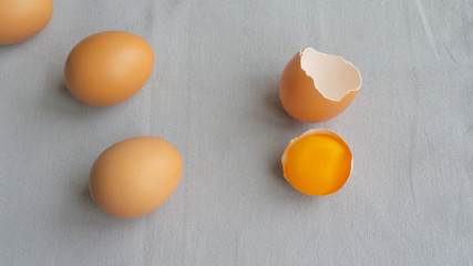 Three chicken brown eggs and one broken egg with yolk in shell on a gray background. Isolated