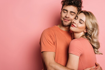 happy young couple embracing with closed eyes on pink background