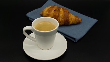 Cup of espresso coffee with a croissant on a blue napkin. Isolated. Black background. 