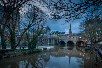 Fototapeta na wymiar Pulteney Bridge with reflection in Avon river with dry tree foreground during twilight at Bath, UK