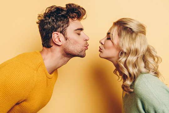 side view of man and woman kissing with closed eyes on yellow background