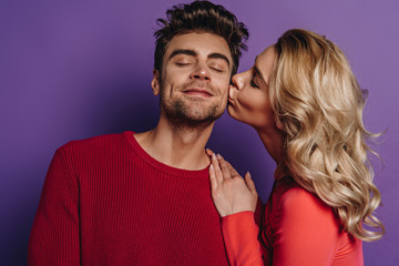 pretty girl kissing happy boyfriend standing with closed eyes on purple background